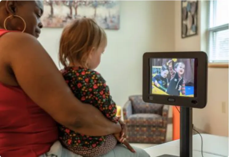 A caregiver holds a young child on her lap while the child watches the EarliPoint device
